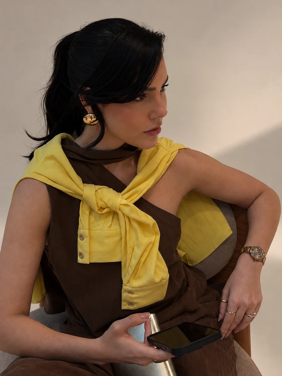 Sabrina Reis com suéter amarelo e celular nas mãos.